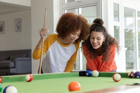 Multicultural friends lining up pool shot at home on green felt table casual recreation
