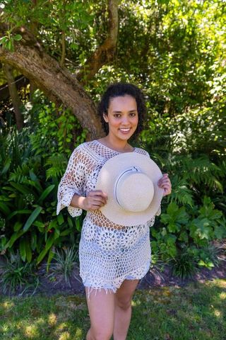 African american woman smiling in shaded garden holding straw hat in crochet cover-up