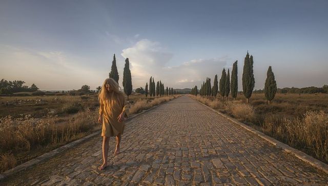Walking barefoot woman on tuscan cypress avenue at golden sunset, solitary mediterranean
