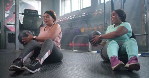 Workout partners training core with medicine balls, smiling and motivating each other in modern gym