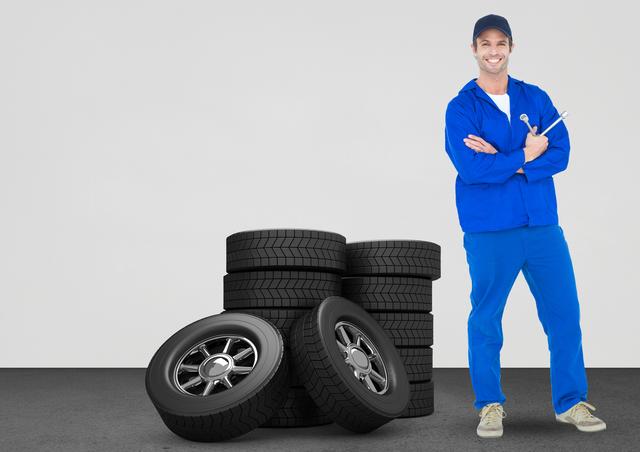 Smiling mechanic holding lug wrench and standing next to tyres against white background