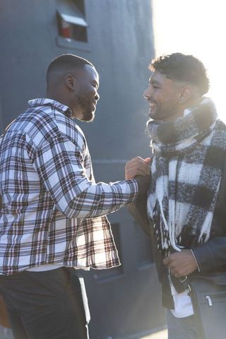 Diverse male friends greeting and smiling outdoors backlit in casual plaid and scarf
