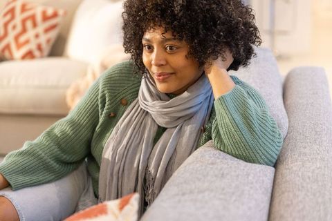 African american woman relaxing on gray sofa in green sweater and scarf, cozy home portrait