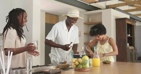 Black friends preparing fresh fruit drinks at kitchen island with rustic wood and straw hat