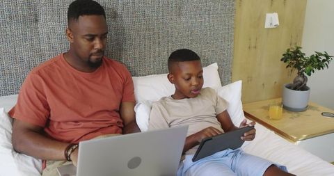 Father and son using devices in modern bedroom