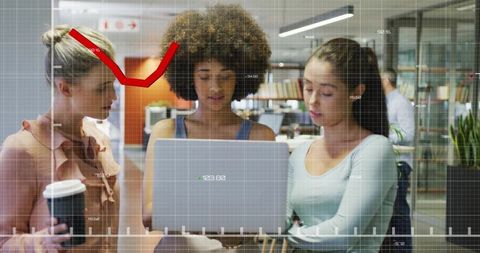 Collaborating women analyzing laptop with data overlay in modern open office workspace