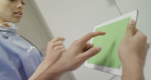 Medical professionals are seen using a tablet with a green screen for navigation, suggesting a healthcare or hospital setting. This can be ideal for depicting modern medical technology use, telemedicine, or training purposes in promotional materials or educational programs.