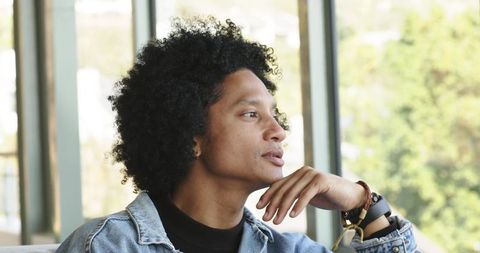 Contemplative african american man gazing out window, resting chin, wearing denim jacket