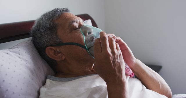 Senior man lying in bed using oxygen mask for breathing support in a healthcare setting. Image suitable for healthcare websites, medical articles, respiratory health resources, and promotional materials for home care services.
