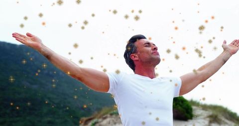 Middle-aged man embracing nature with arms outstretched on sand dune with golden sparkles