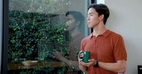 Serene Reflection: Asian Man Enjoying Coffee by Window