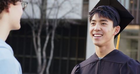 Celebrating graduation: smiling graduate chatting with friend on university campus