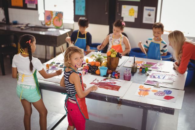 Children are engaged in a lively art class, painting and drawing with various colors. A teacher is assisting them, fostering creativity and learning. This image is perfect for educational materials, school brochures, and articles about creative learning environments.