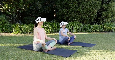 Asian Mother and Daughter Meditating with VR Headsets in Garden
