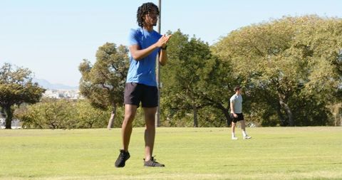 African american athlete lunging and clapping on park field during outdoor team training