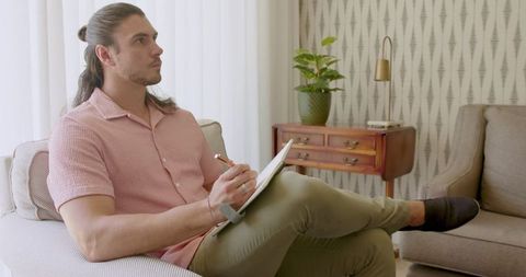 Man Writing in Notebook on Cozy Living Room Sofa with Relaxed Pose