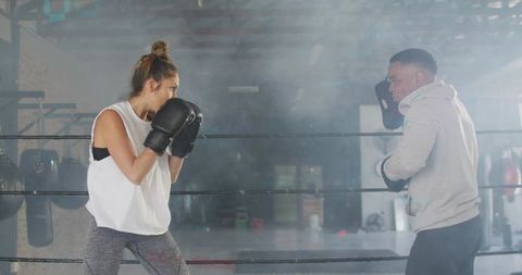 Female boxer jabbing coach mitts in gritty hazy boxing ring