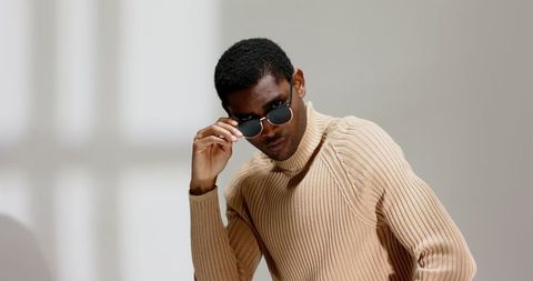 Stylish man in beige turtleneck adjusting sunglasses