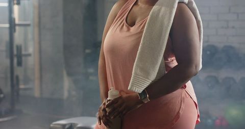 Mid-adult african american woman pausing workout with shaker and towel in gym