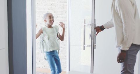 African american father welcoming preteen daughter with backpack through glass door in modern foyer