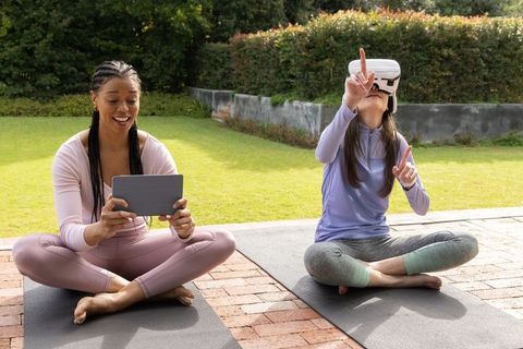 Diverse women practicing outdoor yoga while exploring virtual reality headset and tablet