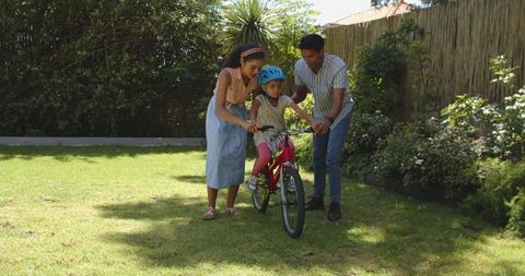 Parents teaching child to ride bicycle in sunny backyard