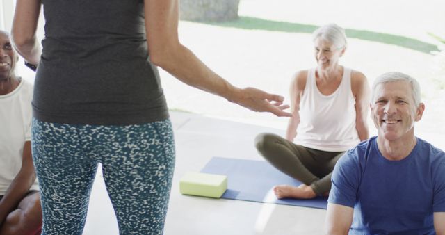 This image depicts a group of elderly individuals participating in a yoga session guided by an instructor in a brightly lit room. This can be useful for promoting wellness programs, senior fitness initiatives, yoga classes targeting older adults, health care, and community recreation events.
