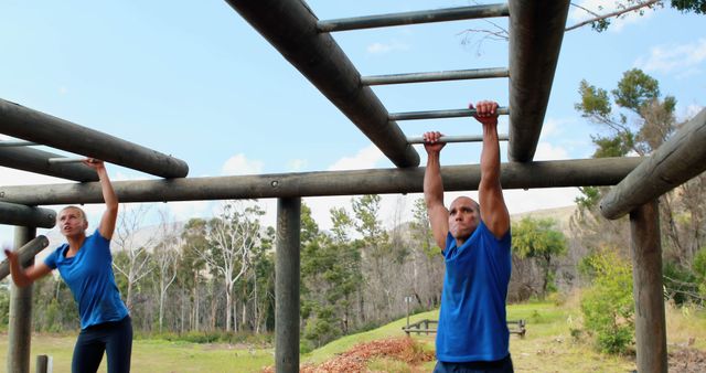 Fit man and fit woman training on monkey bars in an outdoor park, focusing on upper body strength and coordination. Perfect for articles and advertisements related to fitness, outdoor workouts, healthy lifestyle, and exercise regimes in nature settings.
