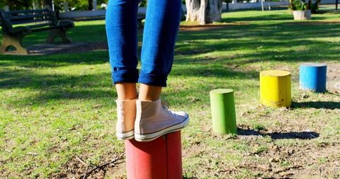 Balancing on colorful park posts wearing pink sneakers and rolled jeans outdoor play and fun