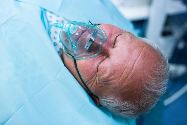 Elderly patient lying on hospital bed with oxygen mask in operation room. Useful for healthcare, medical care, surgery, and emergency treatment themes. Ideal for illustrating patient care, hospital procedures, and medical equipment usage.