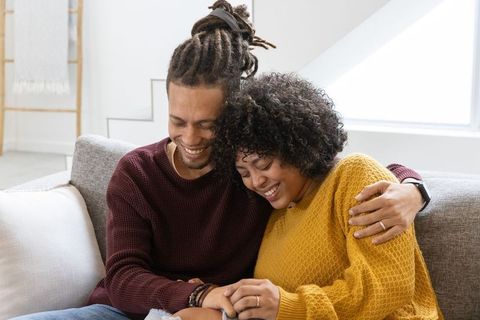 Couple sharing warm embrace on sofa, laughing and holding hands at home