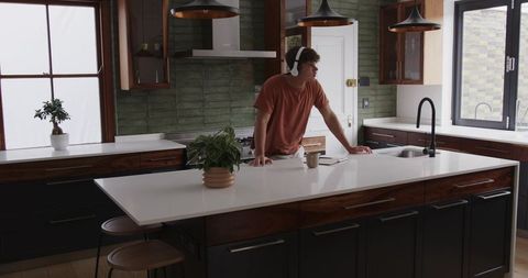Man Listening to Headphones in Modern Minimalist Kitchen Leaning on Island