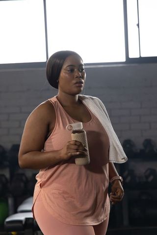 African american woman working out in gym holding water bottle and towel hydrating and determined
