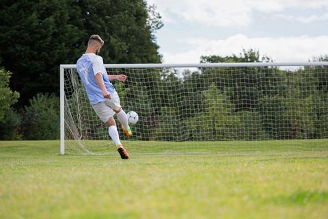 Soccer player kicking ball toward goal on sunny field