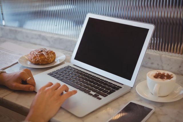 Cropped hands of woman using laptop by coffee cup at counter in cafe