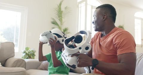 African American father and son exploring virtual reality together on sofa in sunlit living room