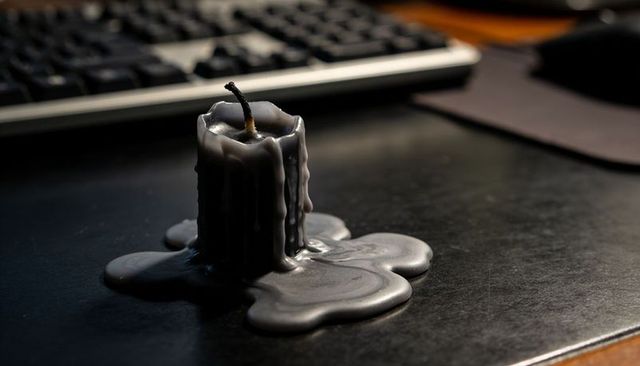 Melting gray candle pooling wax on dark desk with charred wick and blurred keyboard