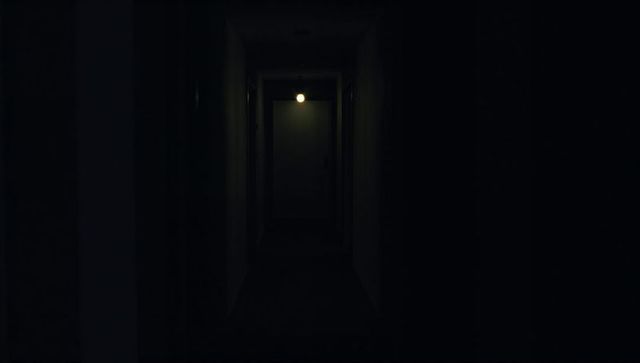 Moody Dark Narrow Hallway Leading to Closed Door with Single Exposed Bulb Lighting
