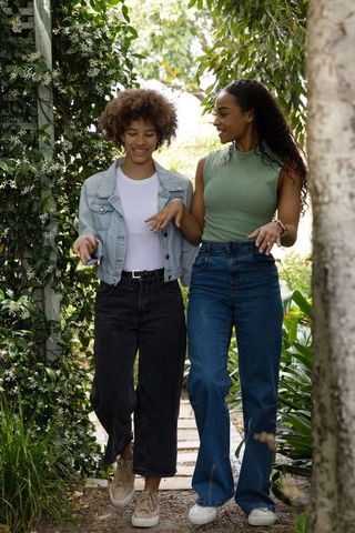 African american friends walking and chatting on sunlit backyard garden path with trellis