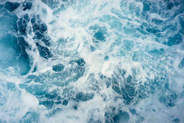 Image captures detailed abstract of turbulent ocean waves with visible foam and intricate texture in shades of blue and aqua. Ideal for use in backgrounds, marine-themed designs, environmental projects, and presentations featuring nature or water-related concepts.