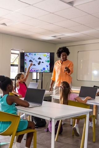 Teacher leading interactive digital lesson with diverse elementary students using laptops