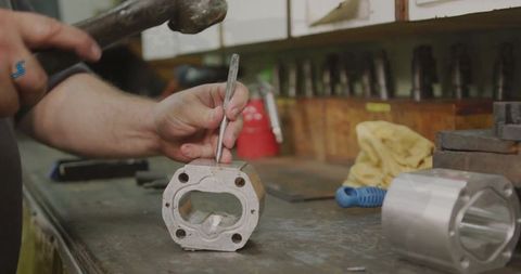 Worker handciof expertly chiseling aluminum block on industrial workbench