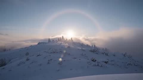 Sunrise Creating 22° Halo Over Snowy Alpine Ridge While Fog Rolls Across Peaks