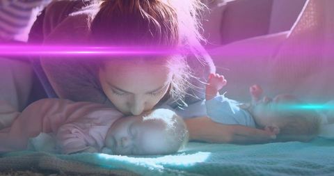 Mother kissing sleeping infant twins on couch with soft backlight and cozy lensflare