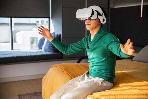 Young man wearing virtual reality headset on bed reacting to immersive gaming experience