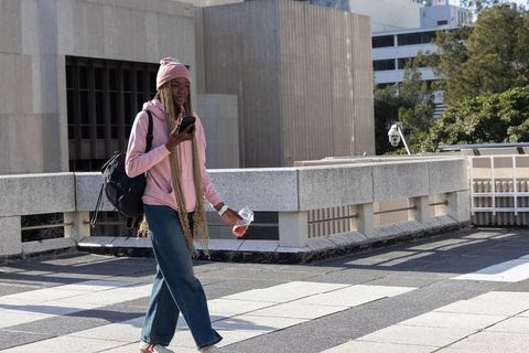 African american woman walking rooftop checking smartphone holding drink urban casual