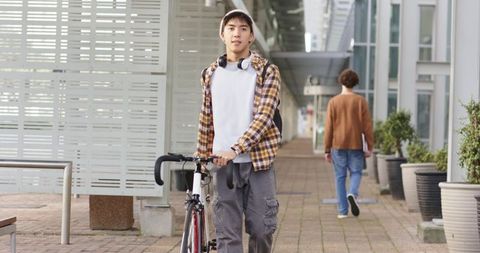 Young commuter pushing road bike through modern glass-lined walkway with headphones