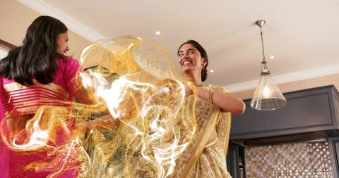 Women dancing and twirling in gold and pink sarees in home kitchen celebration