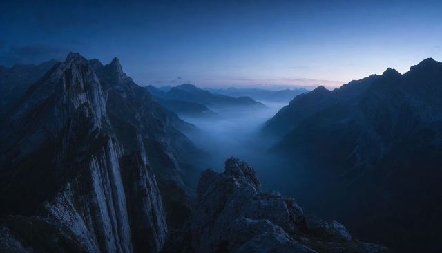Twilight Alpine Ridge Framing Mist-Filled Valley with Distant Dawn Glow