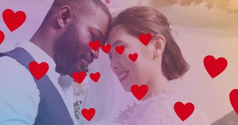 Romantic wedding couple leaning foreheads, smiling with red hearts, veil, vest and floral boutonnier